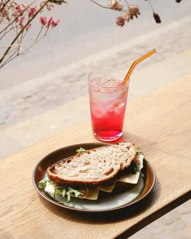 A sandwich and a pink soda in the window light